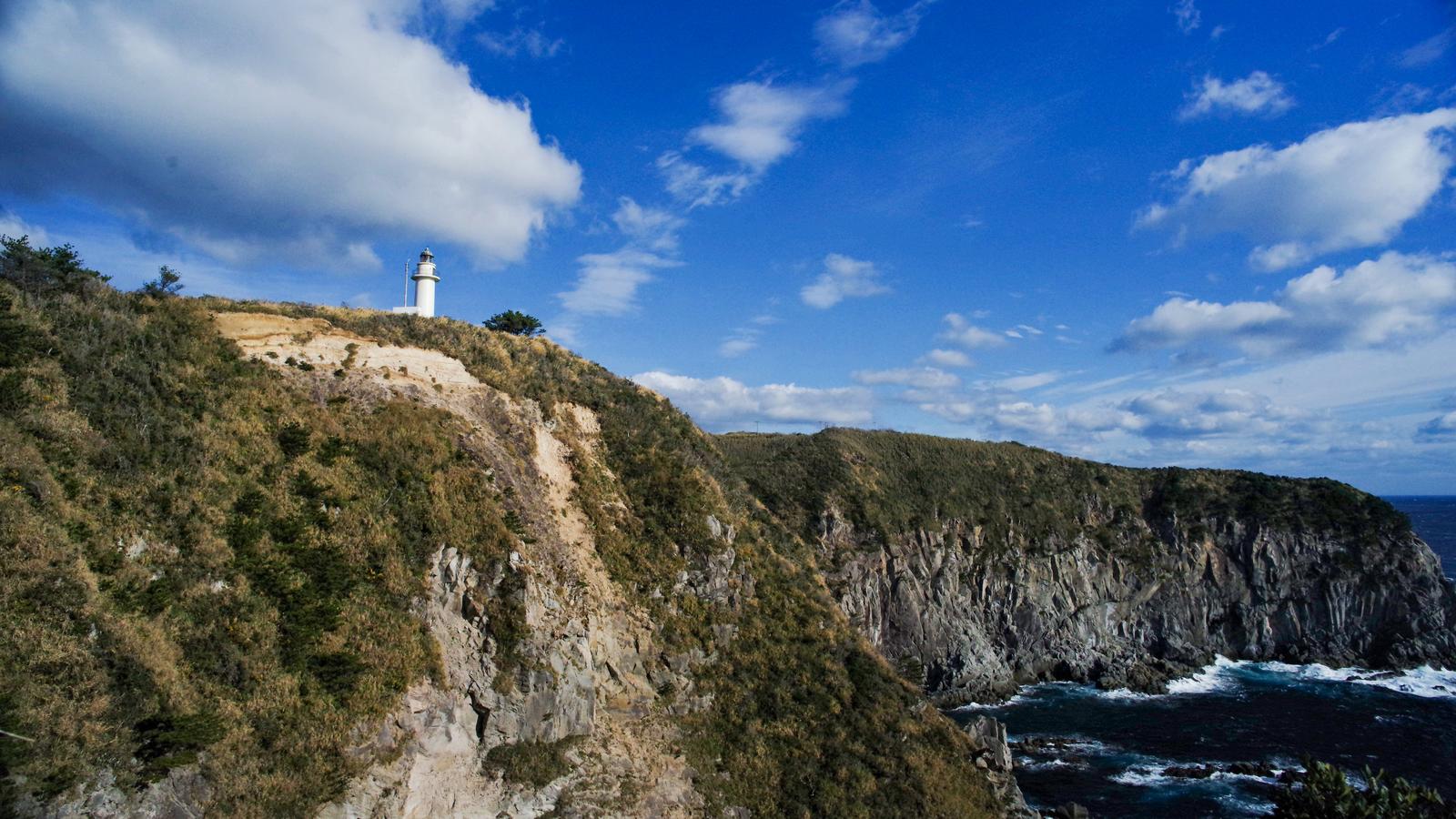 神津島の断崖に立つ白い灯台と青い海、白波の風景