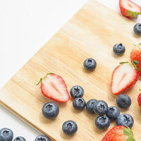 木製まな板に並べたイチゴとブルーベリーのカットフルーツの写真
