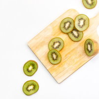 木製まな板の上に薄く輪切りにカットされたキウイフルーツの写真