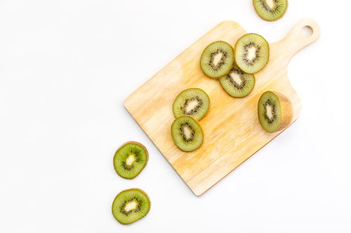 木製まな板の上に薄く輪切りにカットされたキウイフルーツ