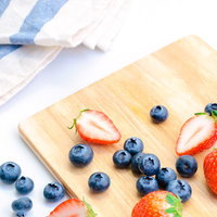 木製カッティングボードに並ぶ甘いイチゴとブルーベリーの写真