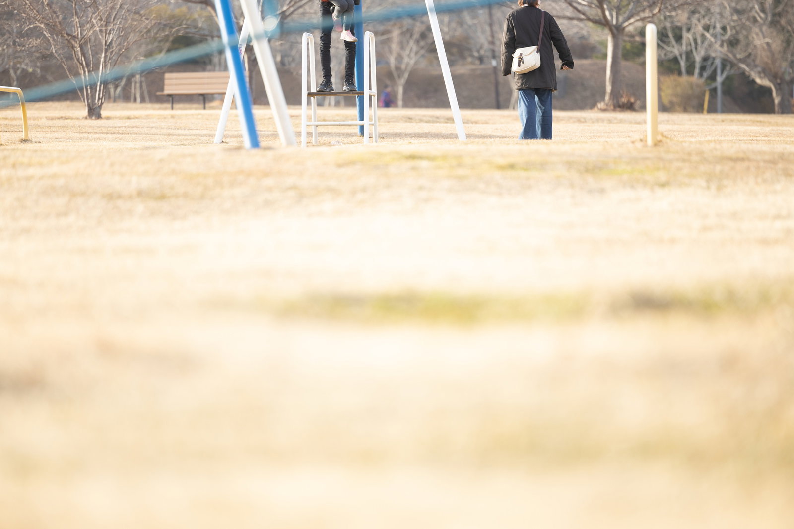 砂地の公園で遊具の前に立つ大人と子ども