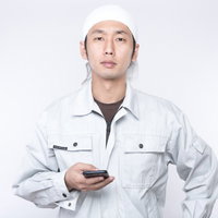 就業中にもかかわらずスマホで遊ぶ作業着姿の若い男性の写真