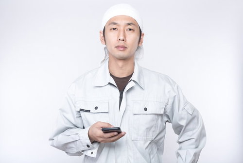 就業中にもかかわらずスマホで遊ぶ作業着姿の若い男性
