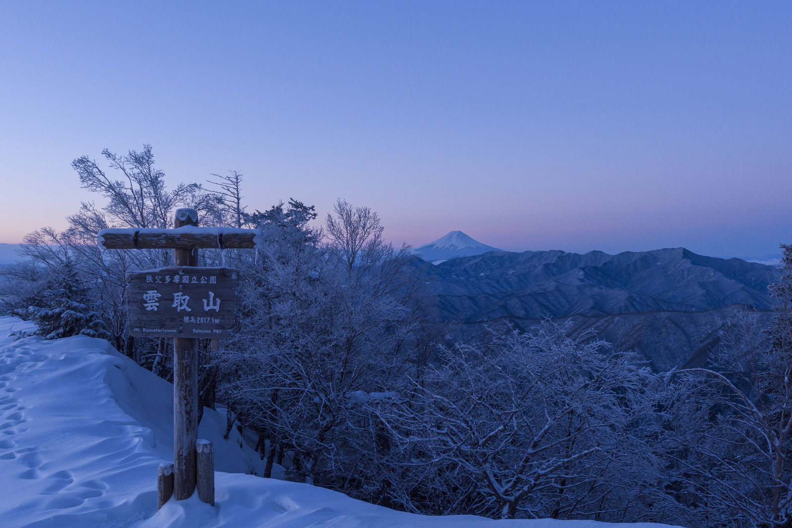 雪化粧した雲取山の山頂標越しに見える富士山と朝焼けの空