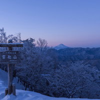 夜明けの雲取山山頂標越しに見える富士山と朝焼けの空の写真