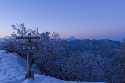 夜明けの雲取山山頂標越しに見える富士山と朝焼けの空