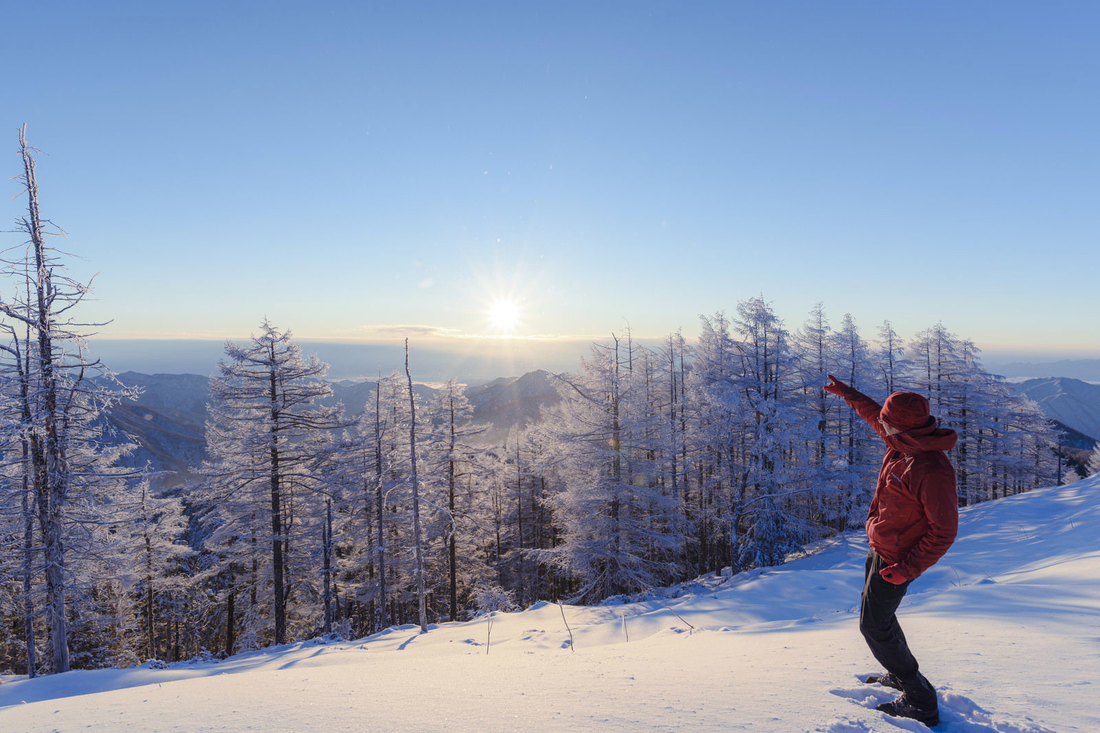 雲取山の雪山で太陽を指差す赤いウェアの登山者と青空