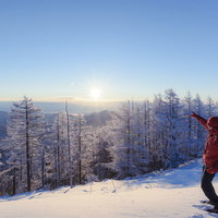 雪化粧した雲取山の山頂で太陽を指差す登山者の写真