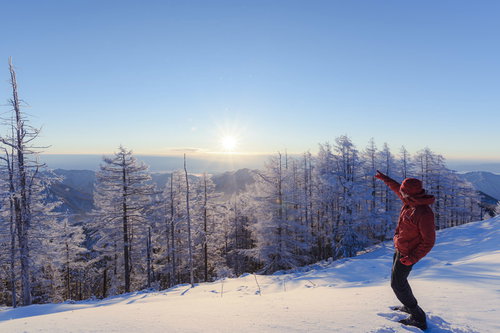 雪化粧した雲取山の山頂で太陽を指差す登山者