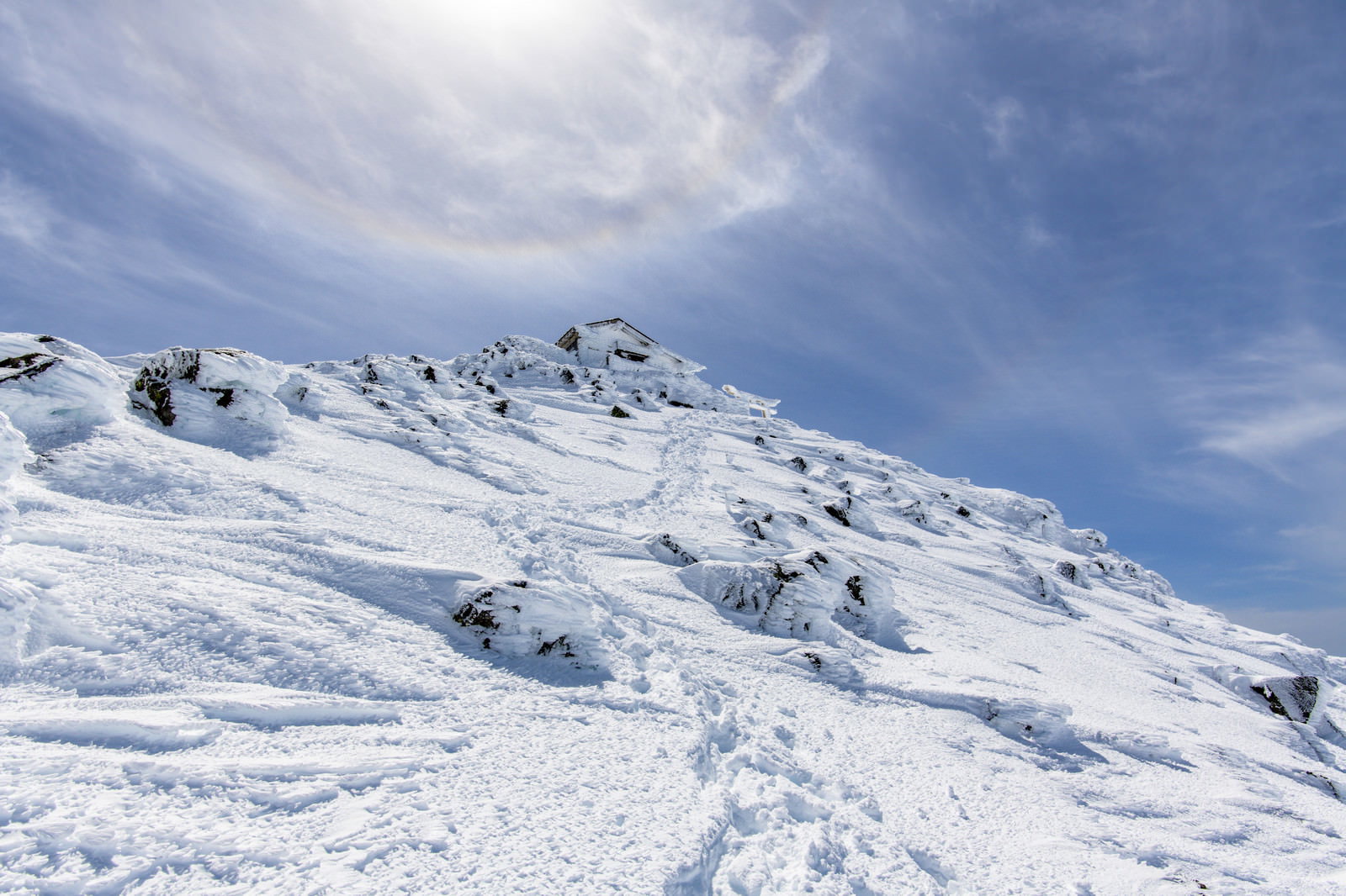 雪に覆われた乗鞍岳山頂の斜面と青空に現れたハロ（暈）の冬山風景