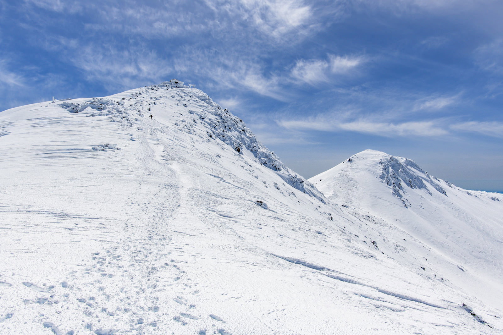青空の下、雪に覆われた乗鞍岳の斜面に山頂へ続くトレースが描かれている