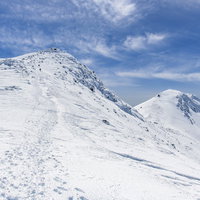 乗鞍岳の雪山、山頂へと続く登山トレースと青空の写真