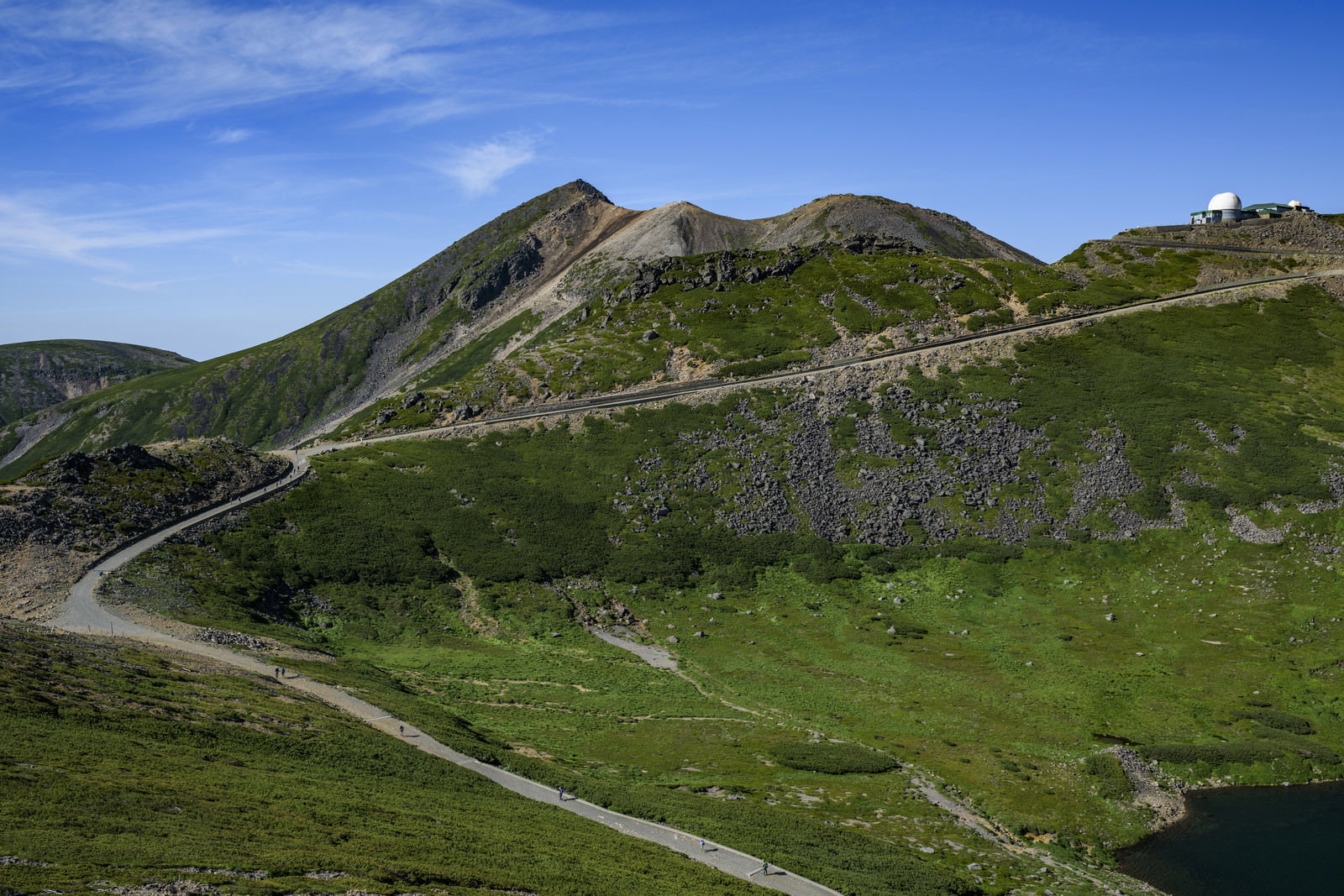 青空の下、緑の山肌に整備された乗鞍岳山頂への登山道