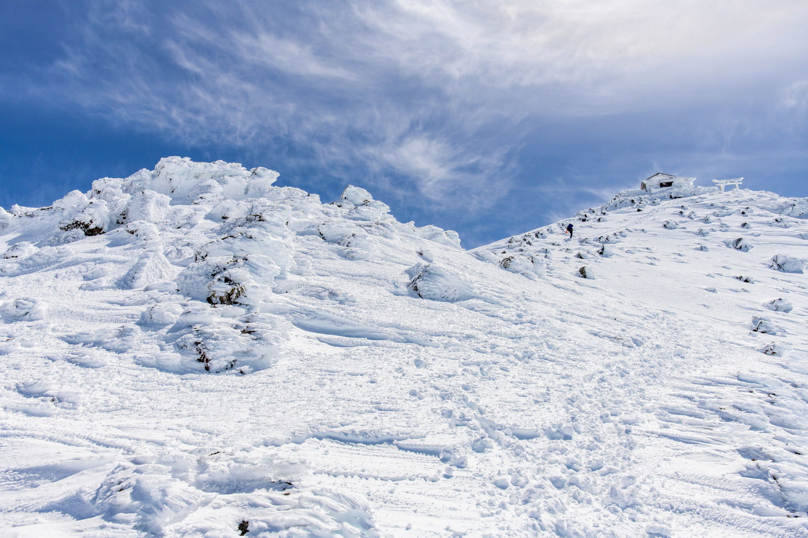 雪化粧した乗鞍岳の山頂付近を歩く登山者と青空に浮かぶ白い雲