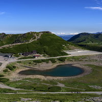 乗鞍岳畳平の権現池と青空、火口湖を囲む緑の高原の写真