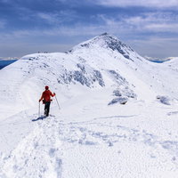 冬の乗鞍岳を登る赤いウェアの登山者の足跡の写真