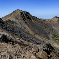 青空の下、岩だらけの乗鞍岳稜線を歩く登山者の風景の写真