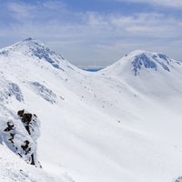 青空の下、雪に包まれた乗鞍岳の山頂と連なる山々の写真