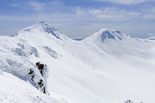 青空の下、雪に包まれた乗鞍岳の山頂と連なる山々