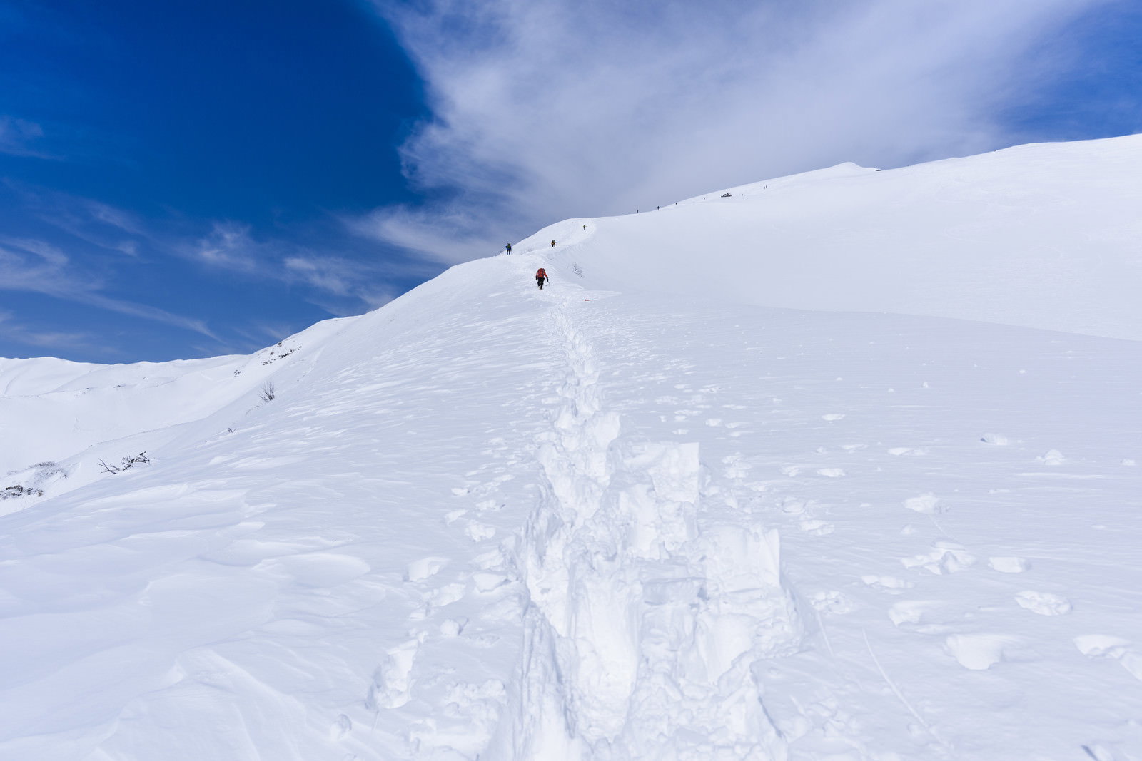 谷川岳の雪山で新雪の中を歩く登山者の足跡と青空