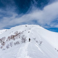 雪化粧した谷川岳の急な斜面を登山者が登る冬の風景の写真