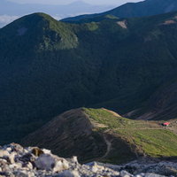 光差す那須岳の避難小屋と連なる山稜と緑の山肌の写真