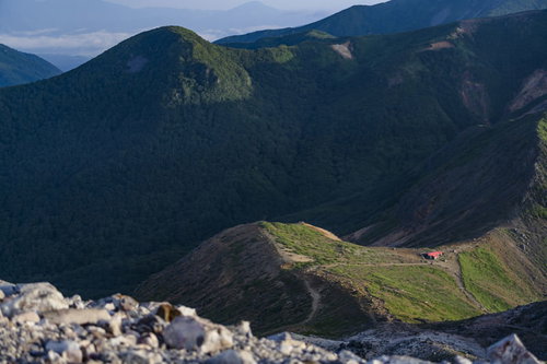 光差す那須岳の避難小屋と連なる山稜と緑の山肌