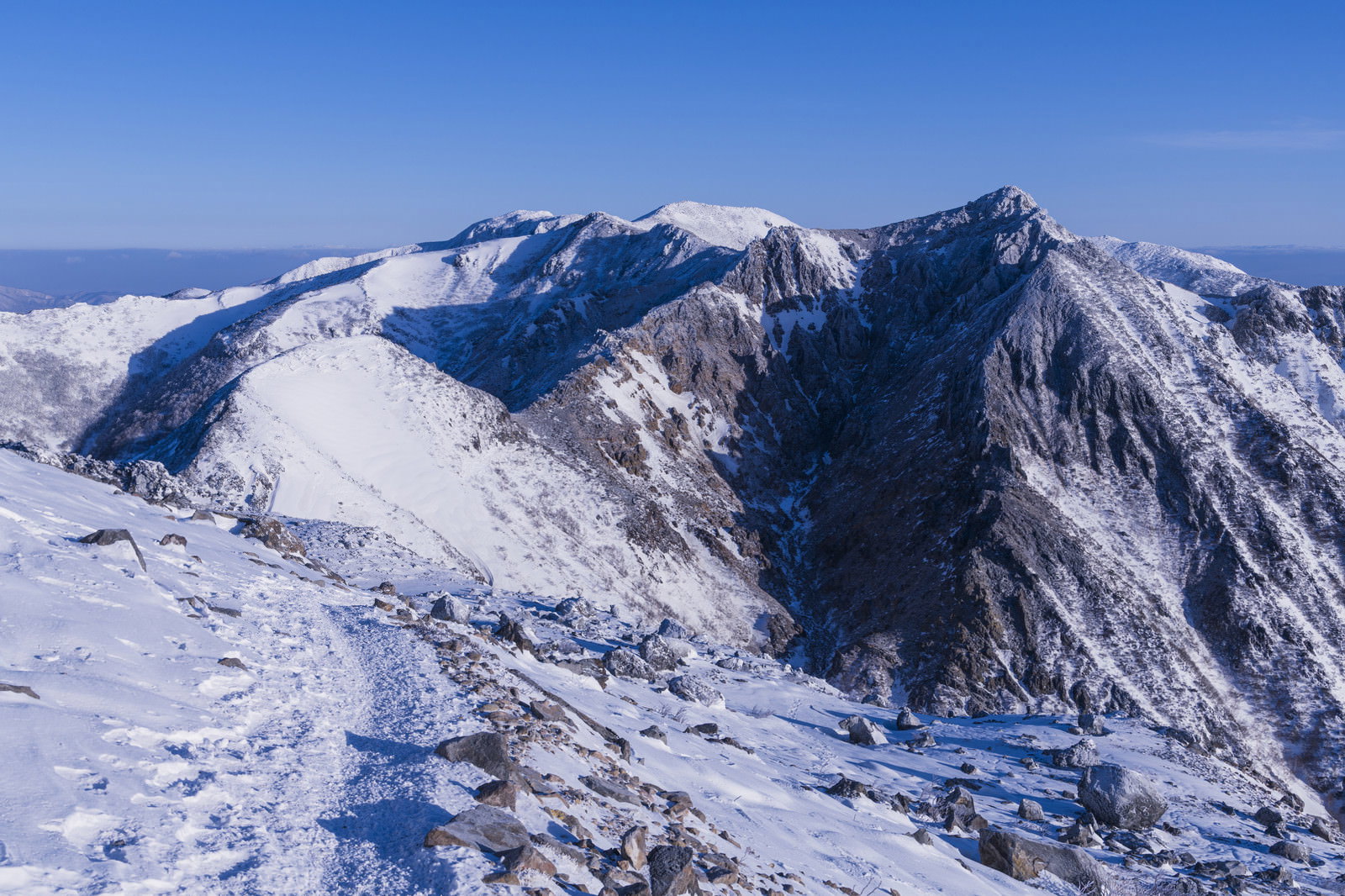 青空の下、雪化粧した那須朝日岳の山頂と周囲の雪山の風景