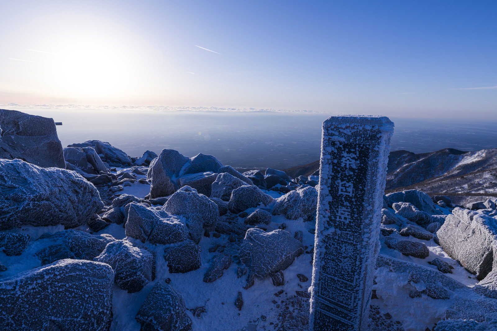 雪に覆われた那須茶臼岳の山頂に立つ山頂標の碑と青空