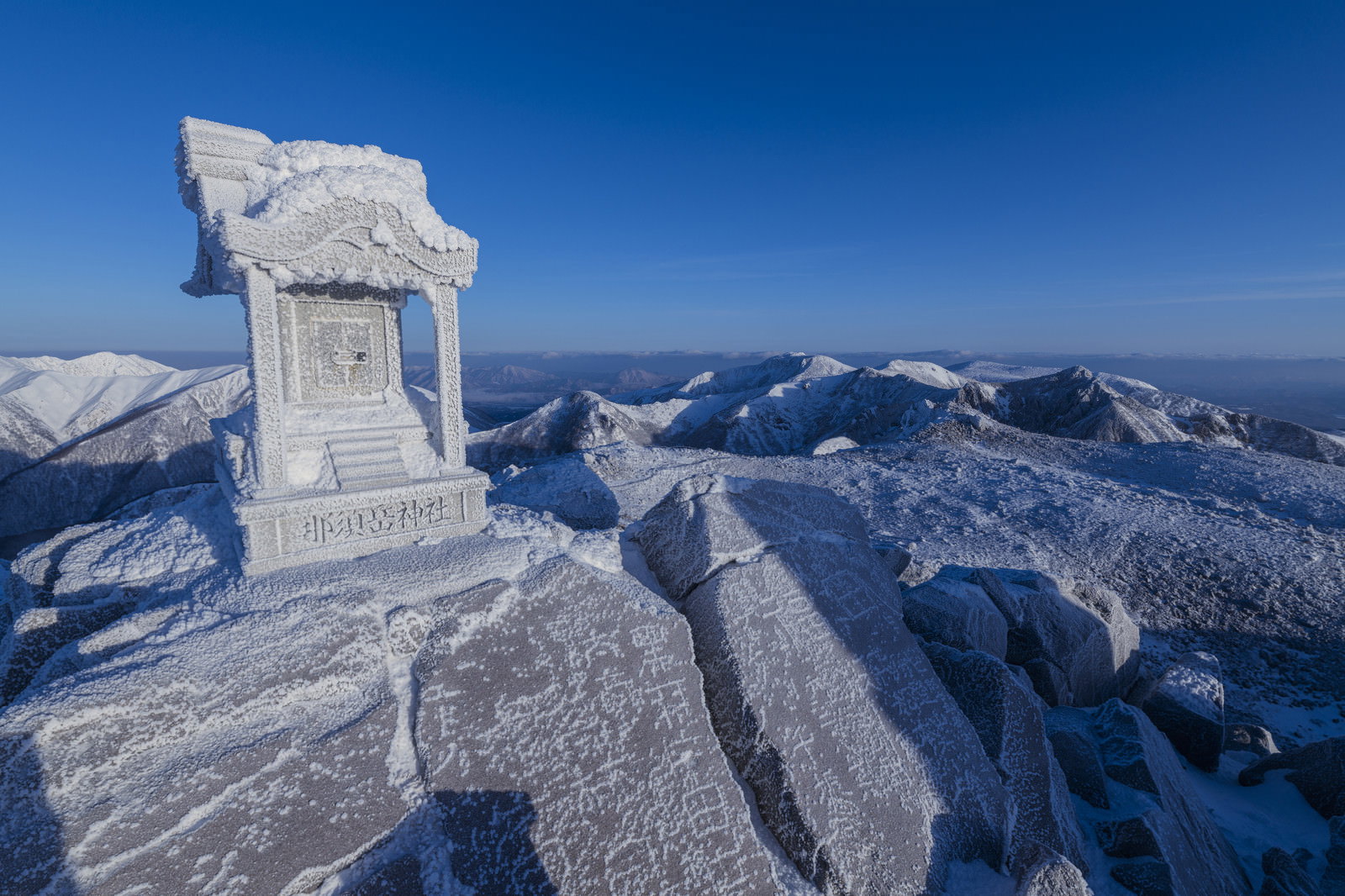 雪と氷に覆われた那須茶臼岳山頂の白い祠と背後の雪山