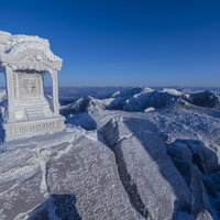 凍り付いた那須茶臼岳山頂の祠と雪化粧の山並みの写真