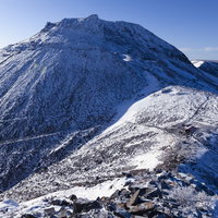 剣ヶ峰山頂から見る雪化粧の那須茶臼岳と冬の山肌の写真
