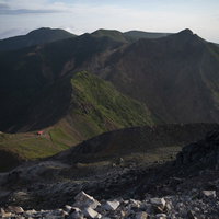 午前の柔らかい光が差す那須岳避難小屋と成層火山の山容の写真