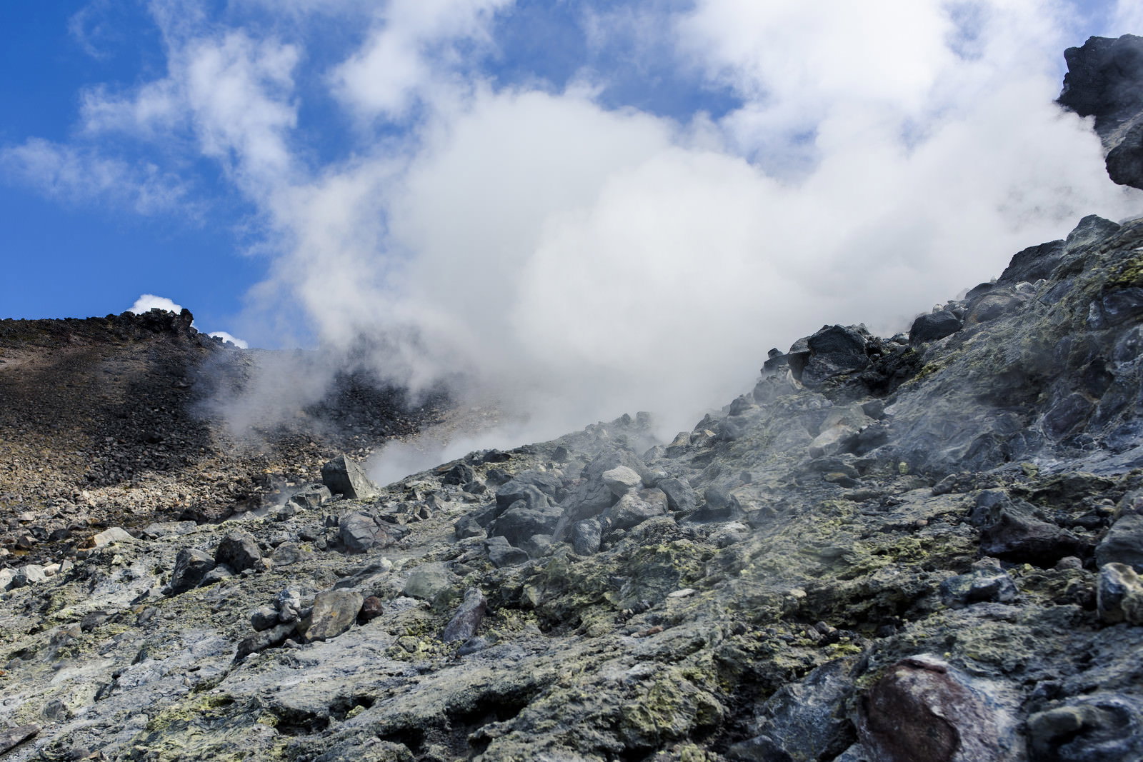 白い噴気が立ち上る那須岳の岩場の登山道