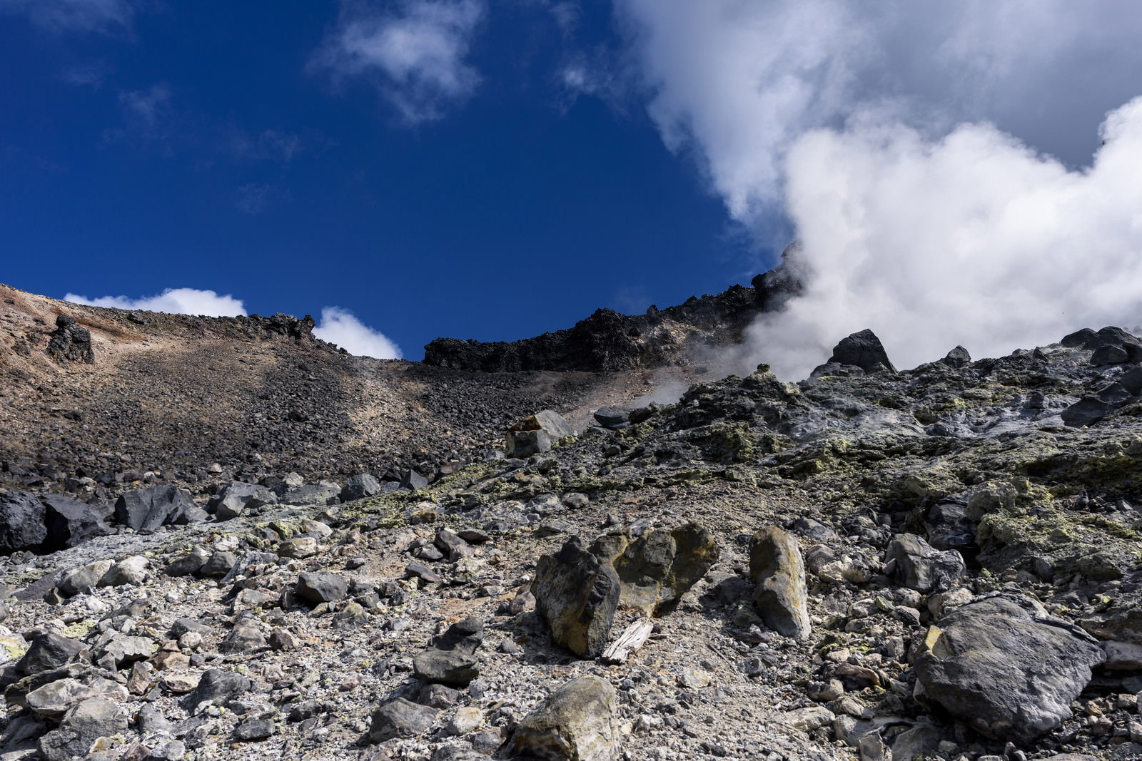 青空の下で白い噴気が立ち上る那須岳の岩だらけの火山地帯