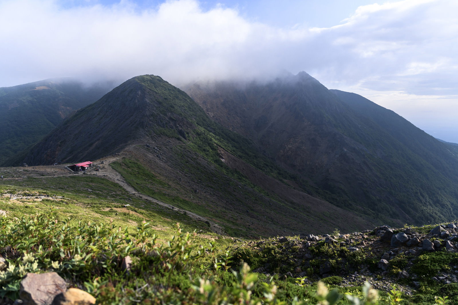 雲に包まれた那須岳の山並みと登山道沿いの山小屋が写る晩夏の風景