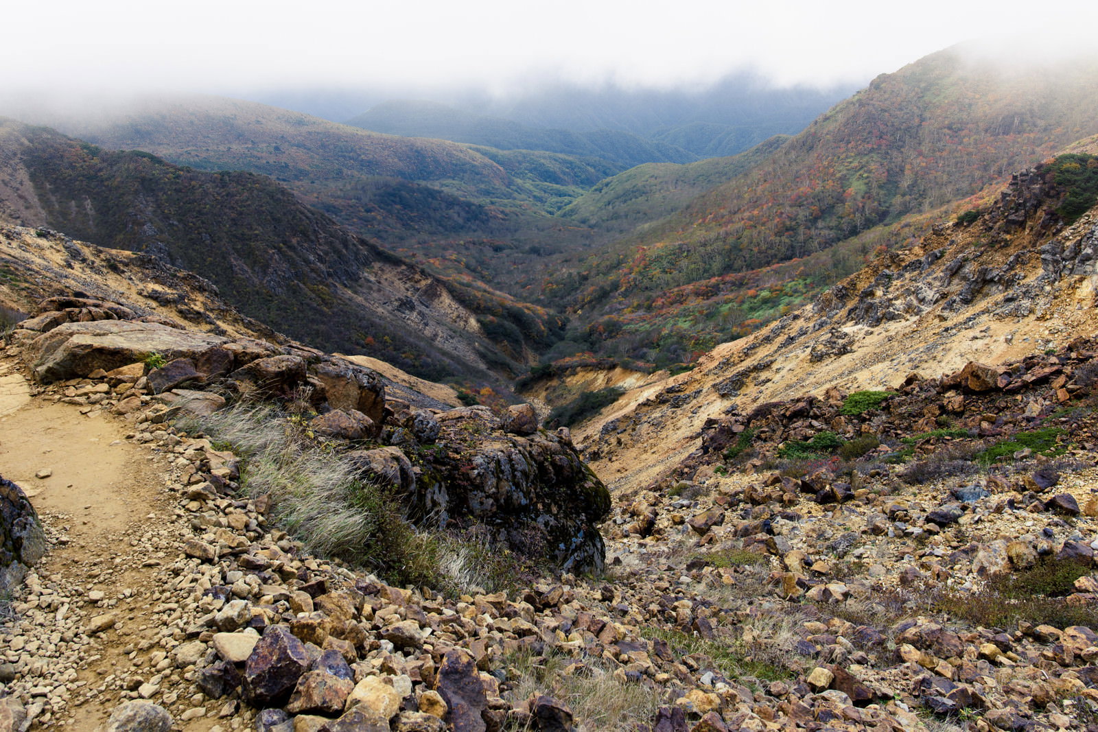 那須岳の火山性岩場と紅葉した樹林帯、遠景に山々の稜線