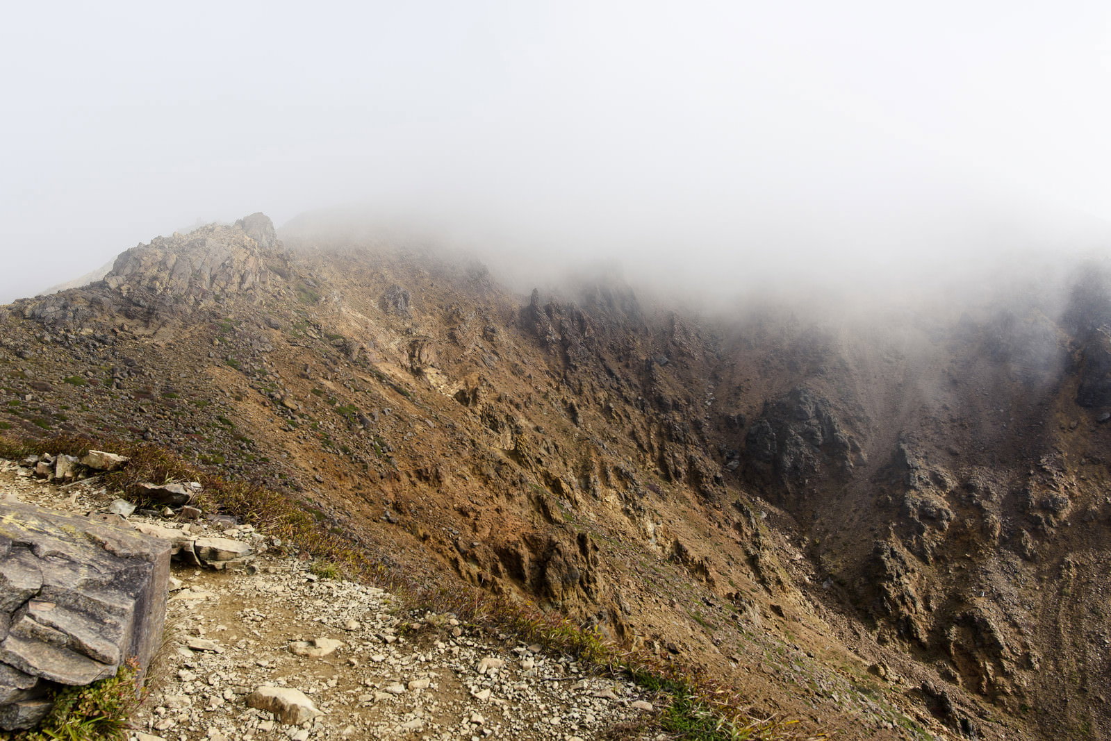 雲に覆われた那須岳の荒涼とした瓦礫の山肌と急峻な崖