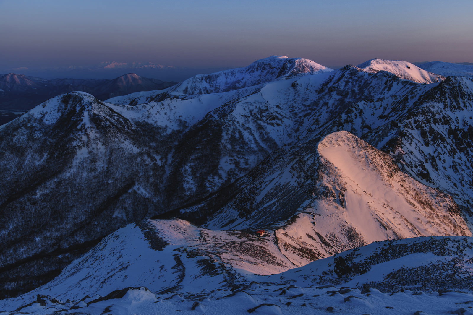 朝焼けに赤く染まった雪山の那須連山と遠景に見える飯豊山
