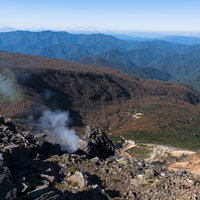 噴気が上がる那須岳の火口斜面と西側の山々の写真