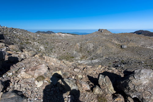 那須岳山頂の岩場に伸びる登山者の影と火山風景