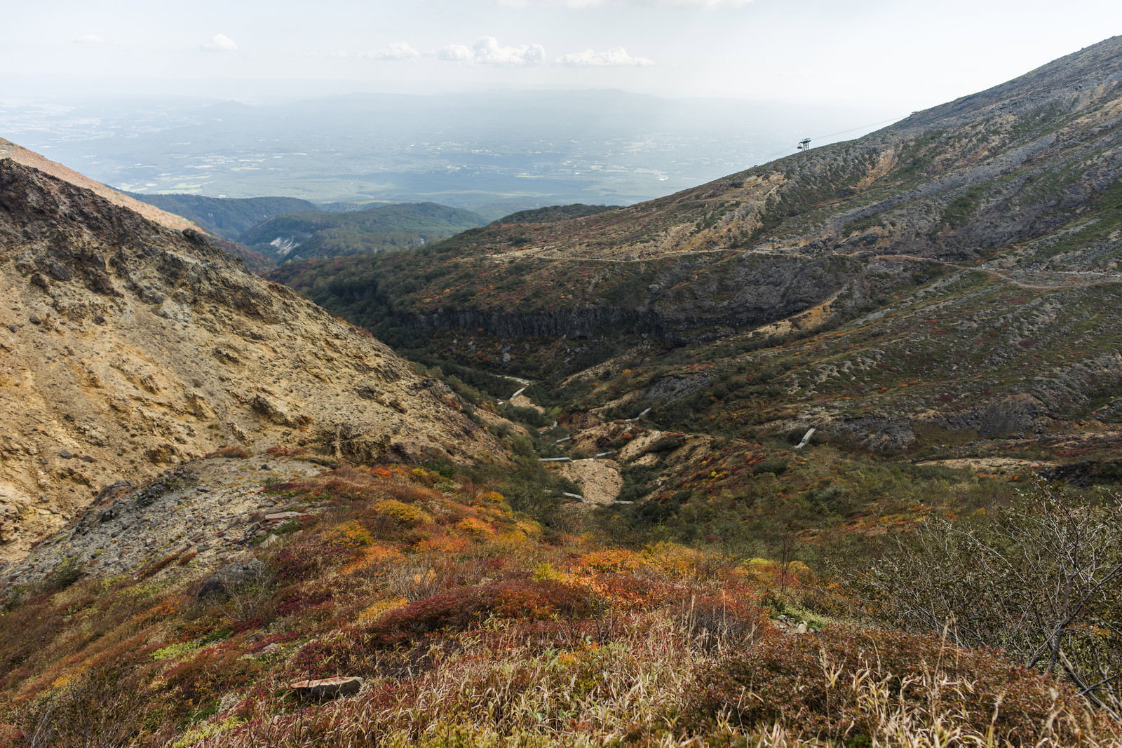 那須岳避難小屋から見た茶褐色の山肌と緑の谷間、遠方の街並み