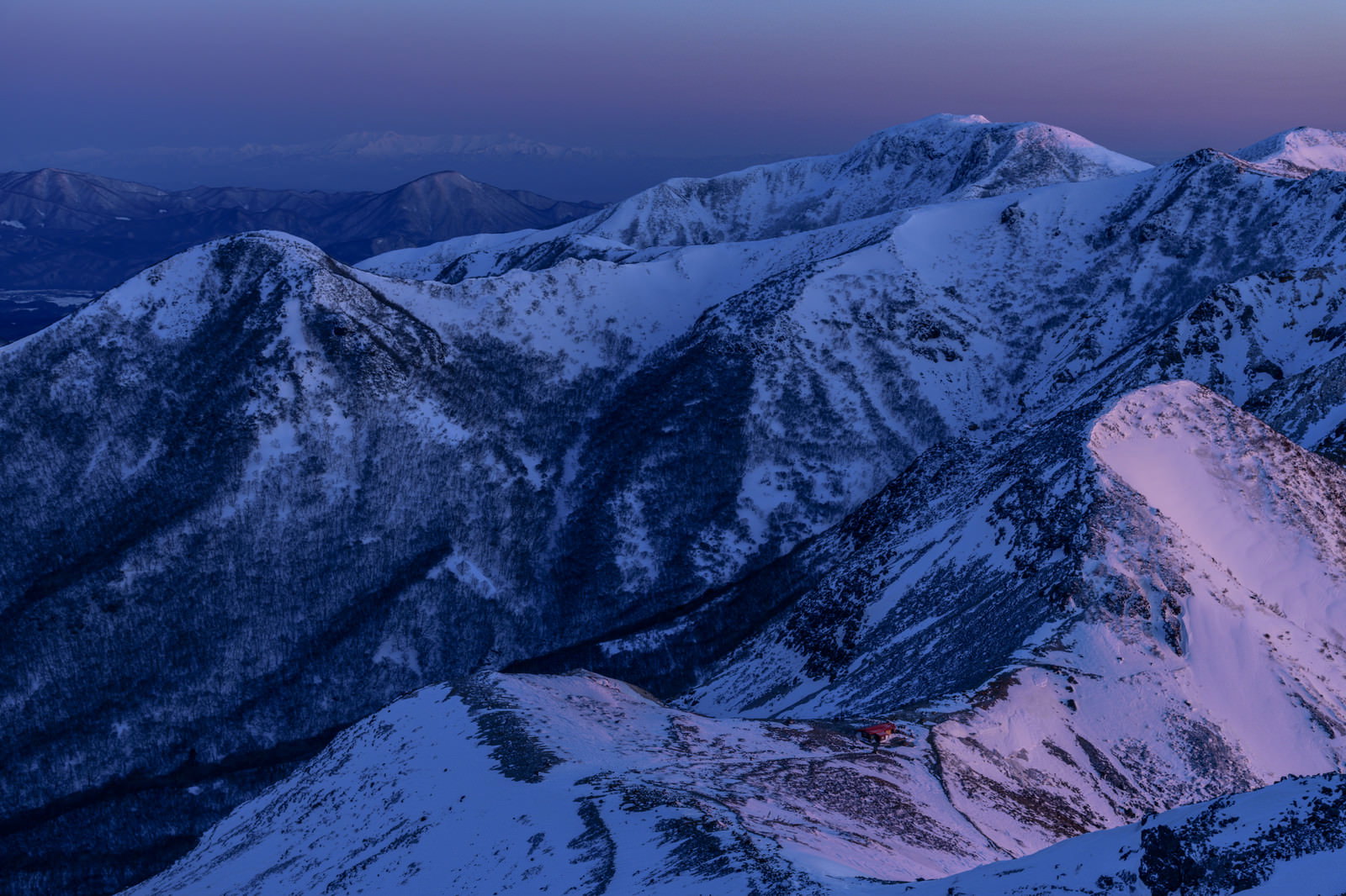 紫色の夕空の下、雪に覆われた那須連山の稜線と避難小屋