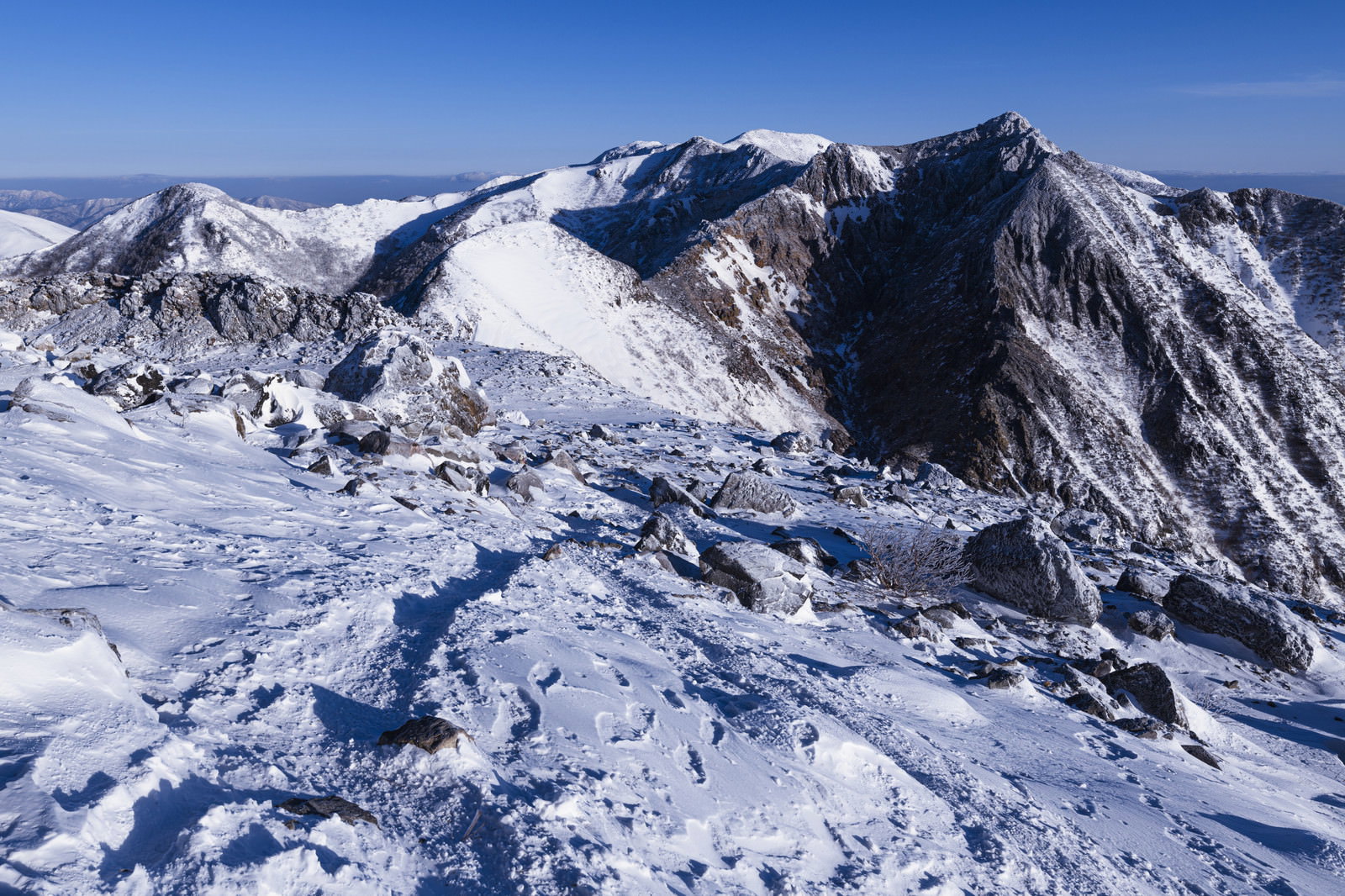 青空の下、雪に覆われた那須岳の山頂部と岩稜が連なる冬山の風景