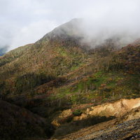 雲の隙間から色づく那須岳の紅葉と成層火山の秋景色の写真
