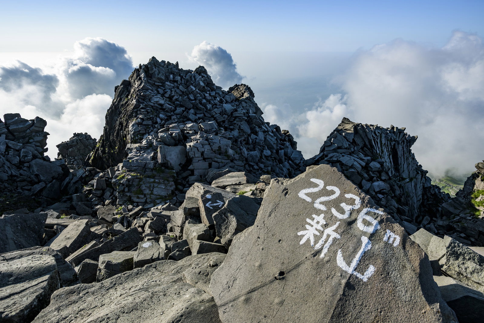 鳥海山山頂の新山2236m標識と険しい岩場、雲海と青空の風景
