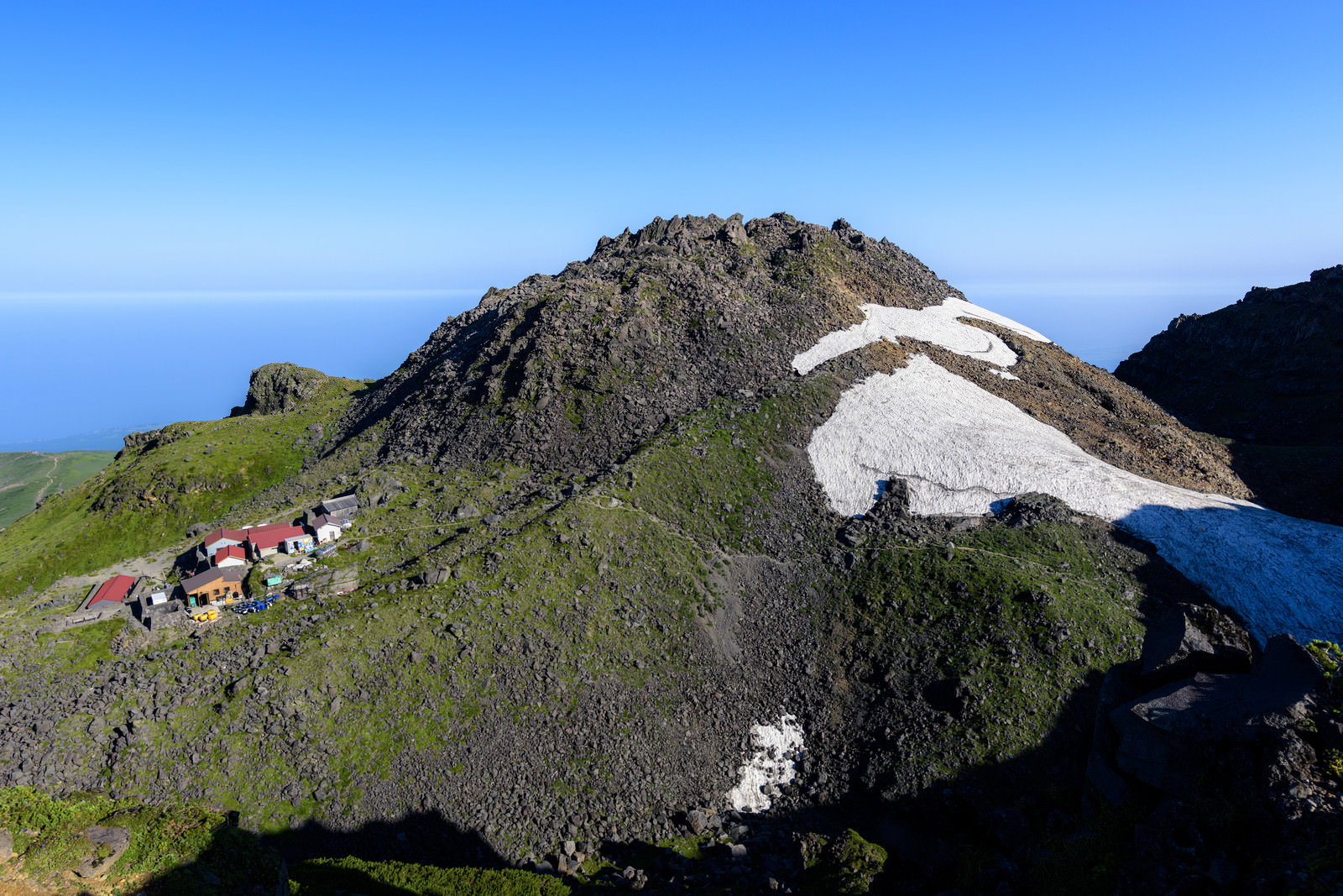 青空の下、鳥海山の岩場の山頂を歩く登山者たち