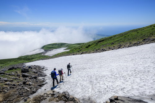 青空の下、鳥海山の雪渓を下る登山者たちの夏山トレッキング