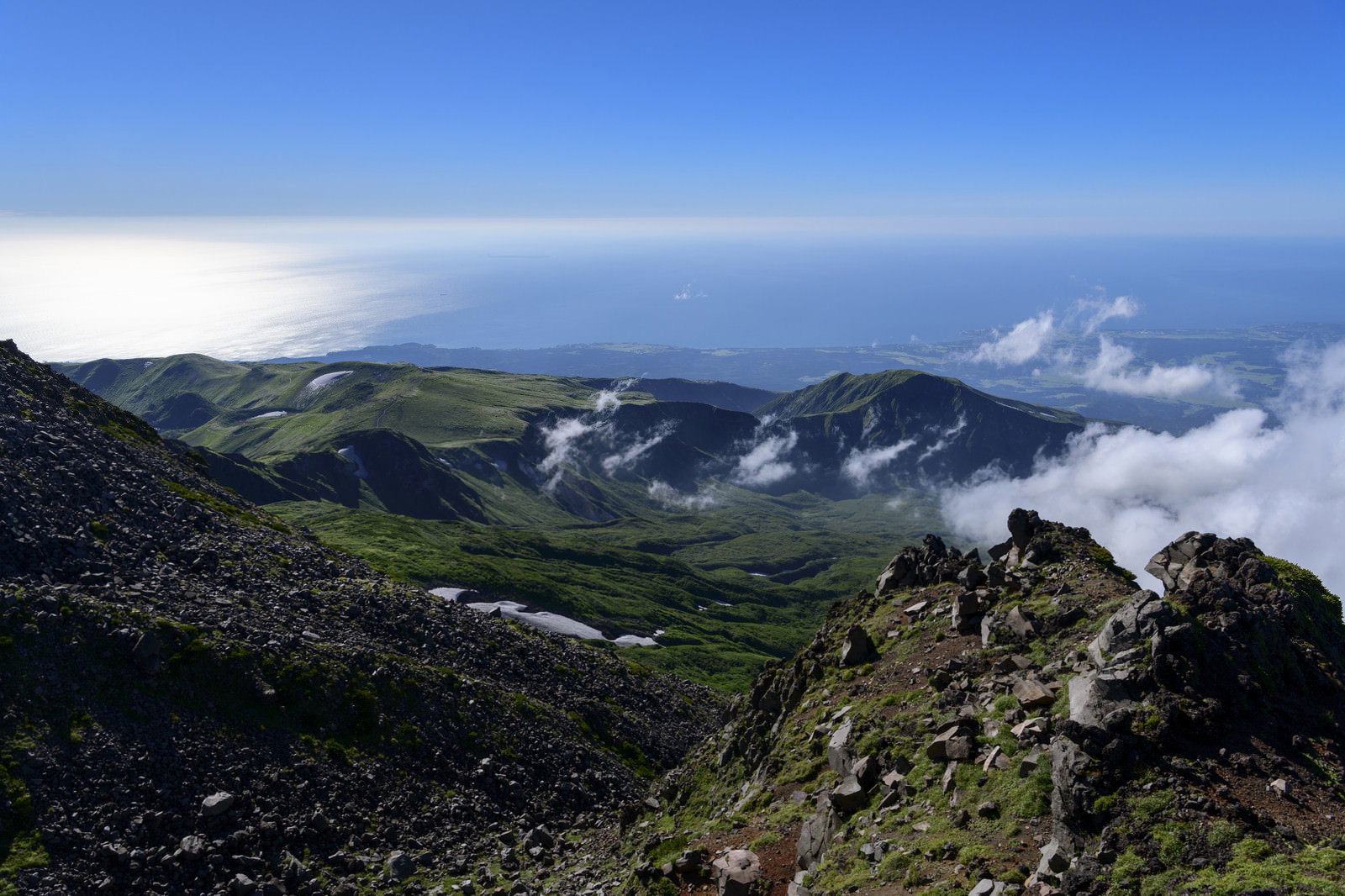 鳥海山七高山の岩場から見下ろす緑の山々と雲海、遠方に日本海が広がる景色